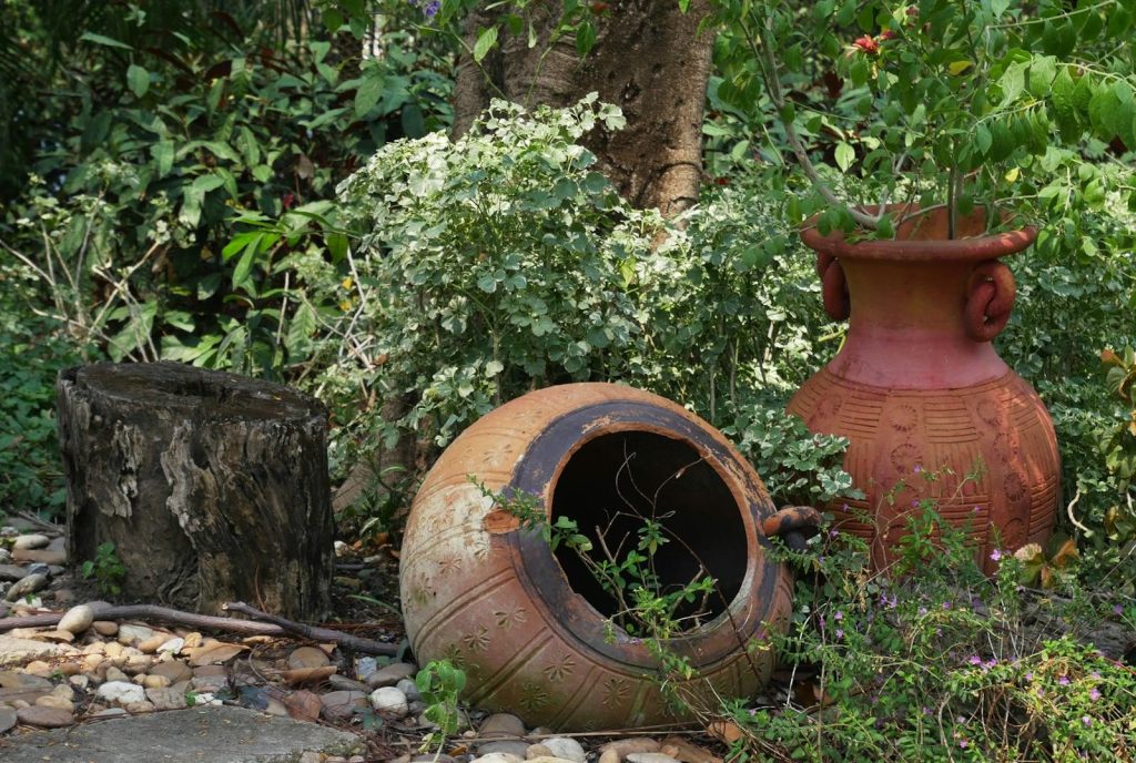 Charming garden setting with clay pots, tree stump, and lush greenery.
