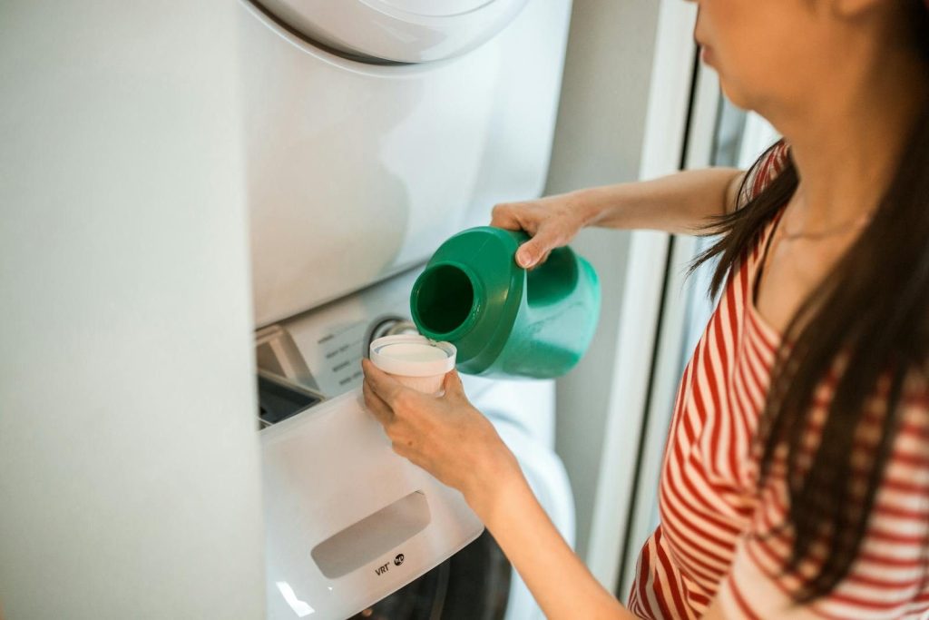 A woman pours detergent into a washing machine in a home laundry room.
