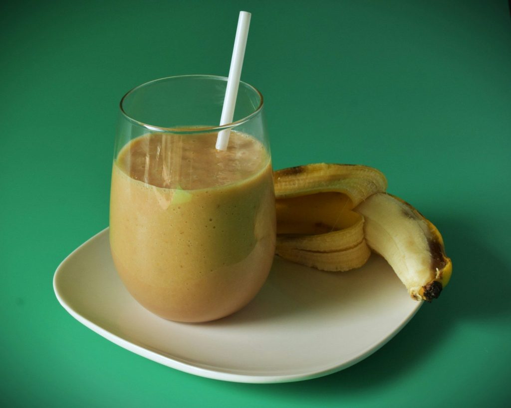 Banana smoothie with a straw and banana on plate