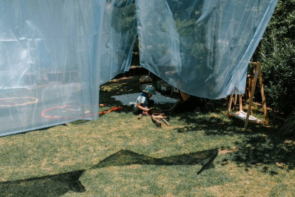 Person sitting under blue netting in a grassy yard.