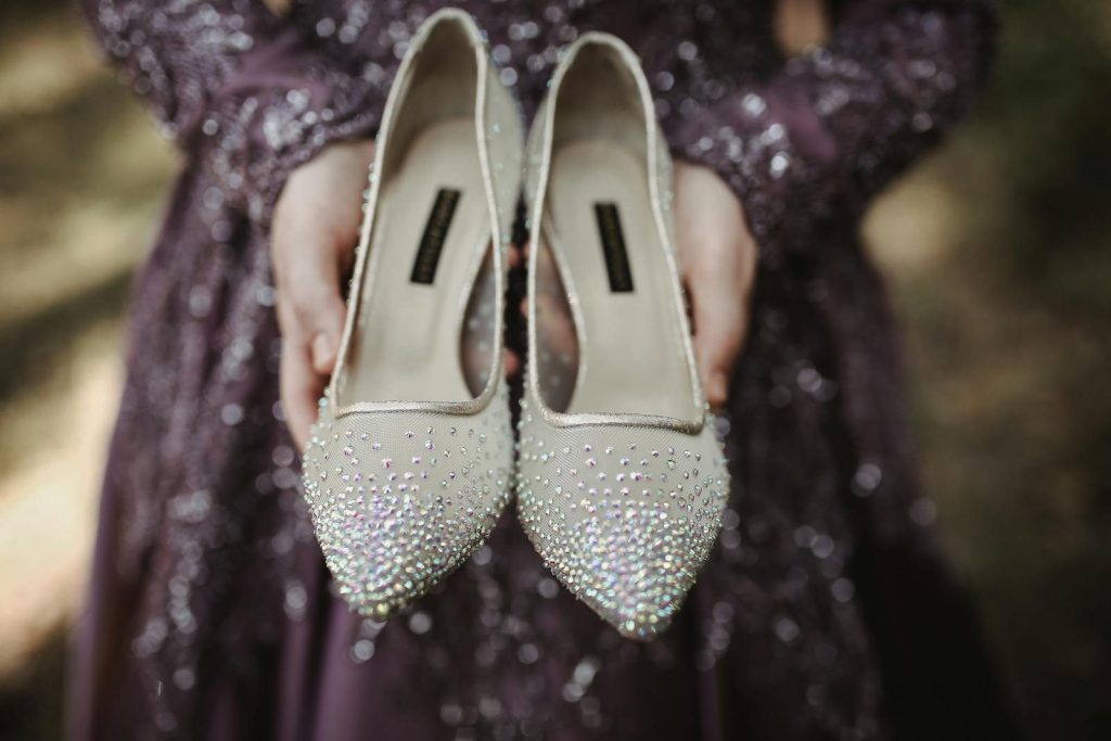 Woman in purple sequin dress holding sparkling high heels outdoors.