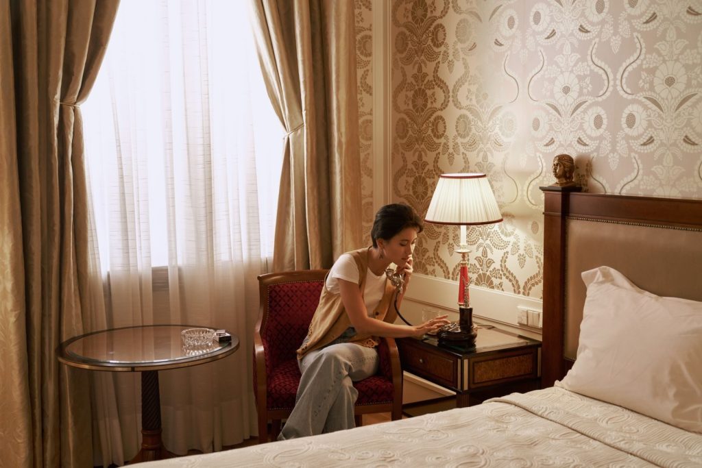 A woman talks on a vintage phone in a luxurious hotel room, creating a retro ambiance.