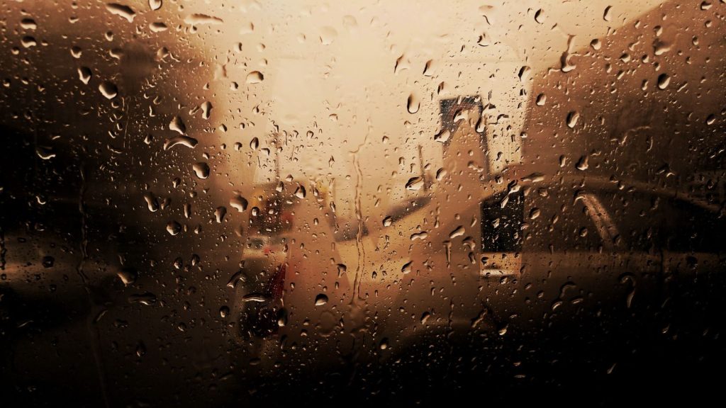 Artistic view of raindrops on a car window with blurred vehicles in the background, creating a moody atmosphere.