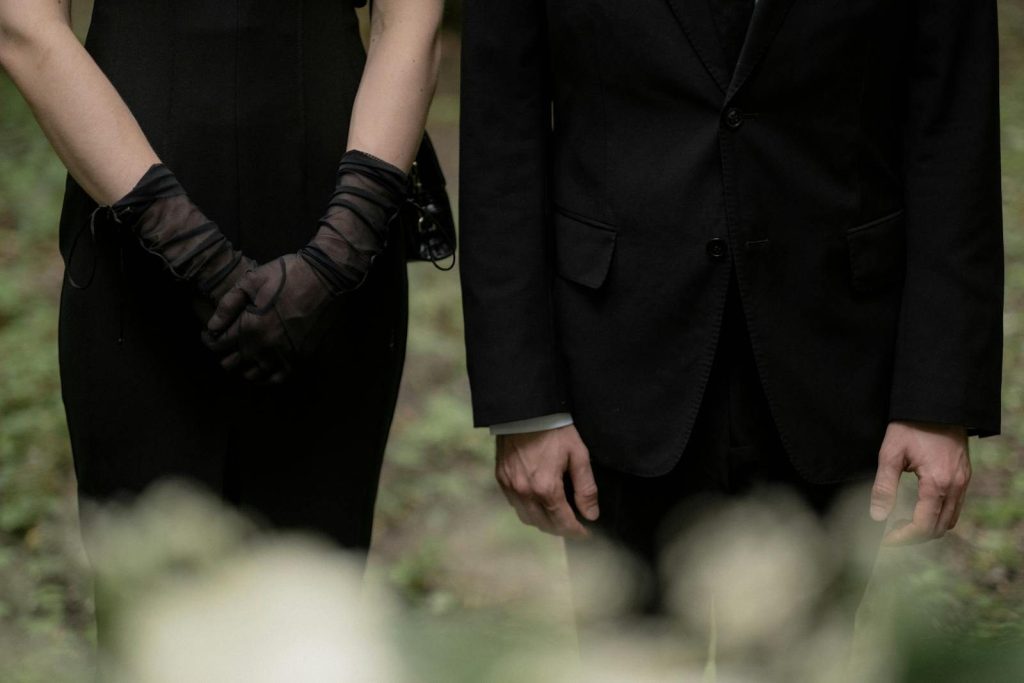 A man and woman in black formal wear stand side by side, exuding a somber mood.