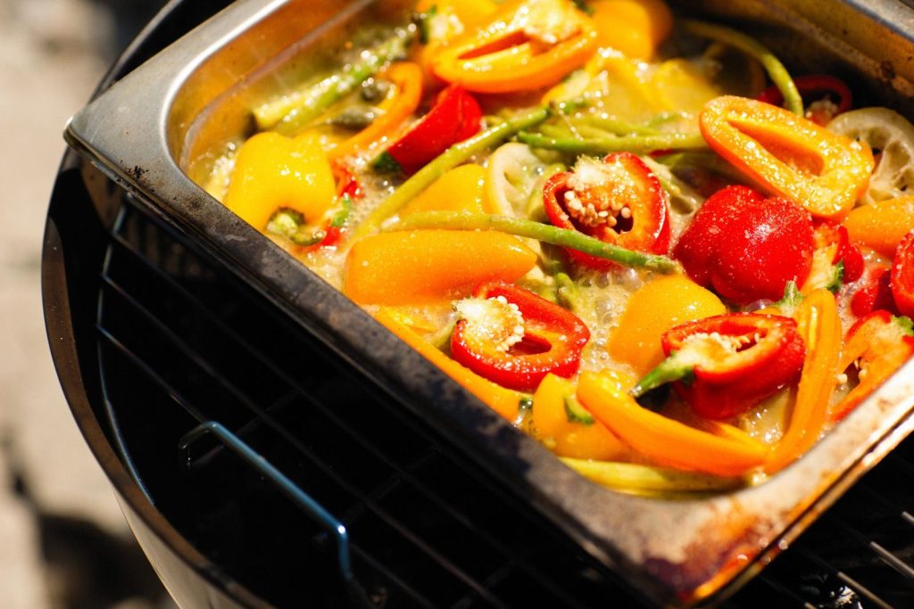 A colorful dish of red and yellow bell peppers grilling in a tray outdoors.