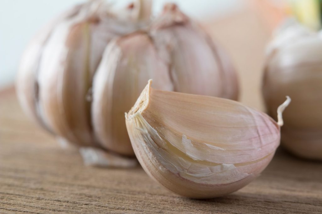 A detailed view of a fresh garlic clove and bulb on a wooden surface. Perfect for food and health themes.