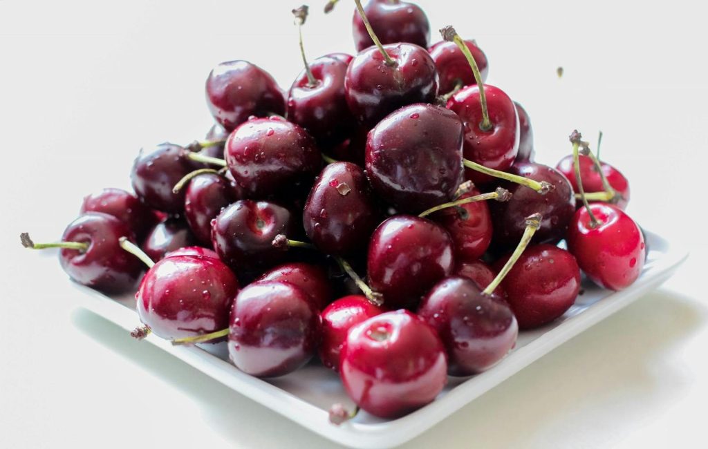 A pile of ripe, juicy red cherries on a white plate, showcasing their freshness.