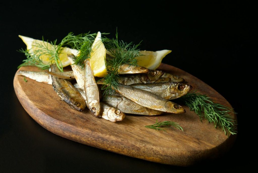 Delicious fresh anchovies laid out on a wooden board with lemon slices and dill.