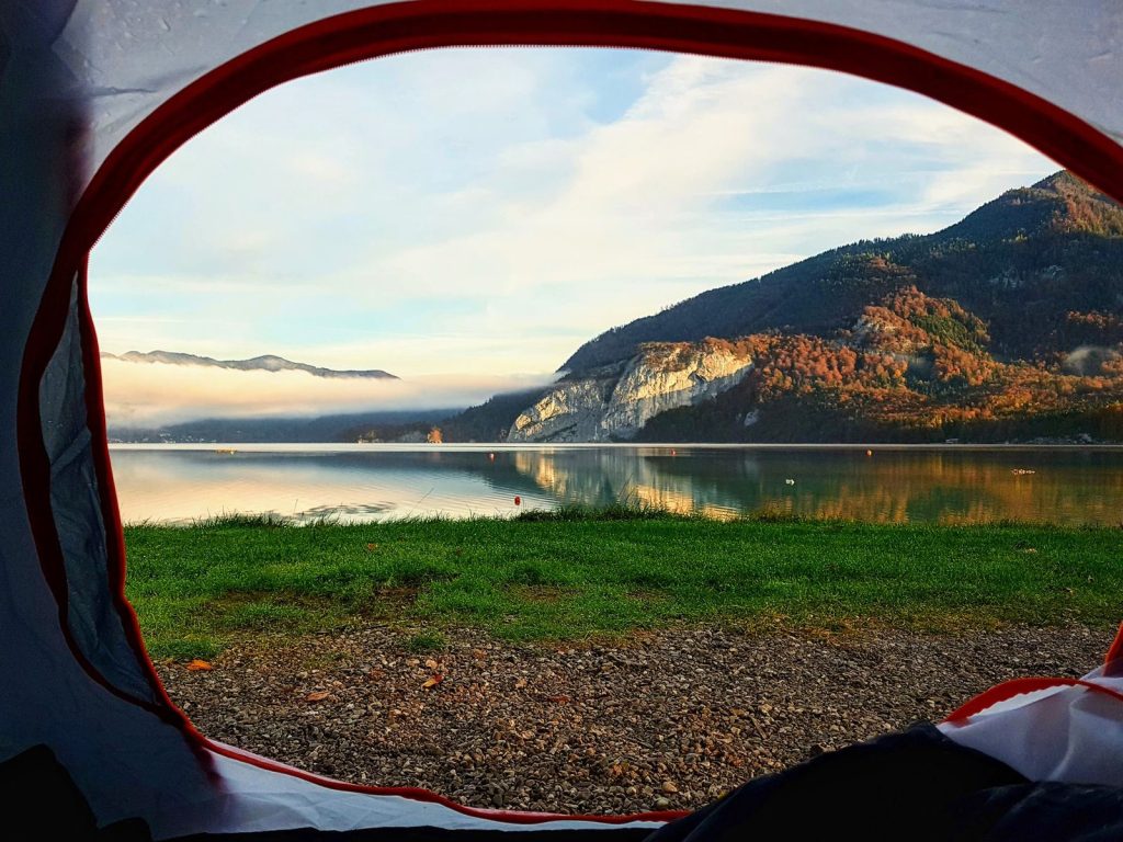 Peaceful camping site with a stunning view of a lake and mountains through a tent opening.