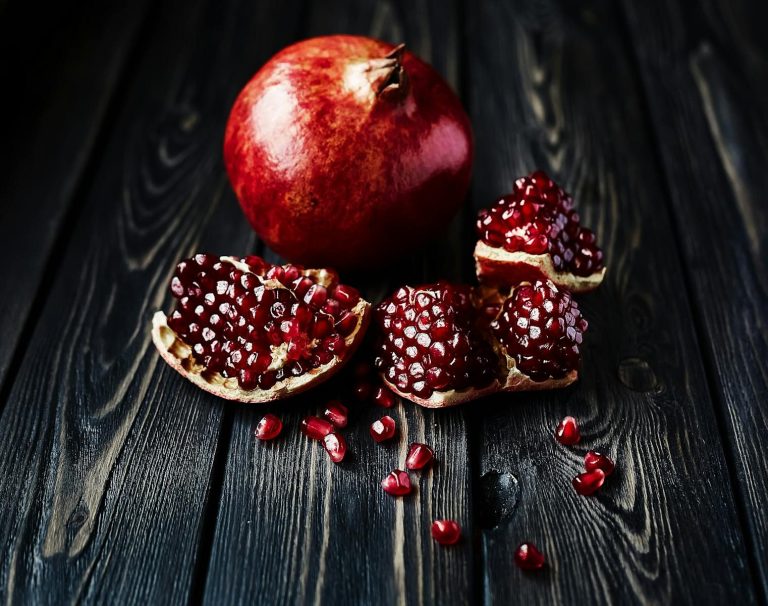 Vivid close-up of fresh organic pomegranate on a rustic wooden surface with scattered seeds.