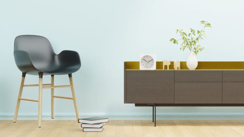 Stylish minimalist interior featuring a modern chair, stack of books, clock, and a vase on cabinet.