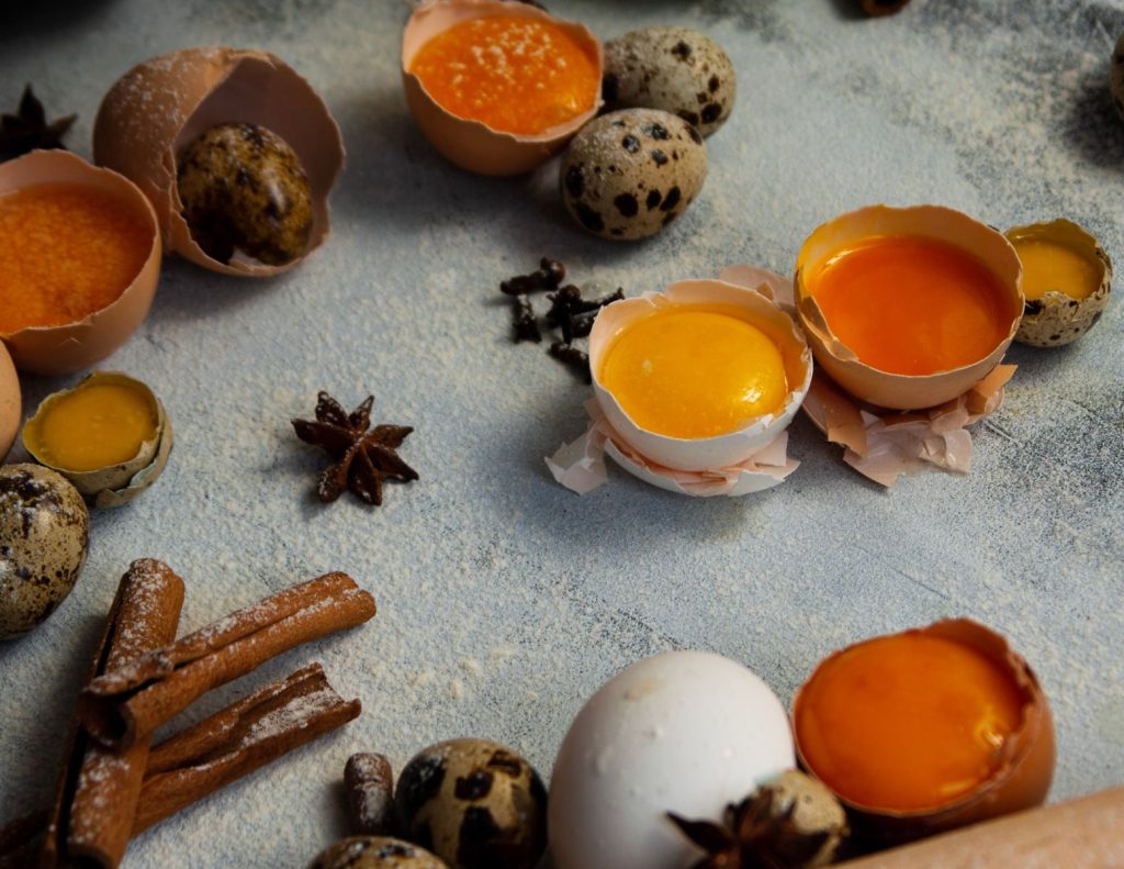 Assortment of quail eggs, spices, and broken eggshells on textured surface.