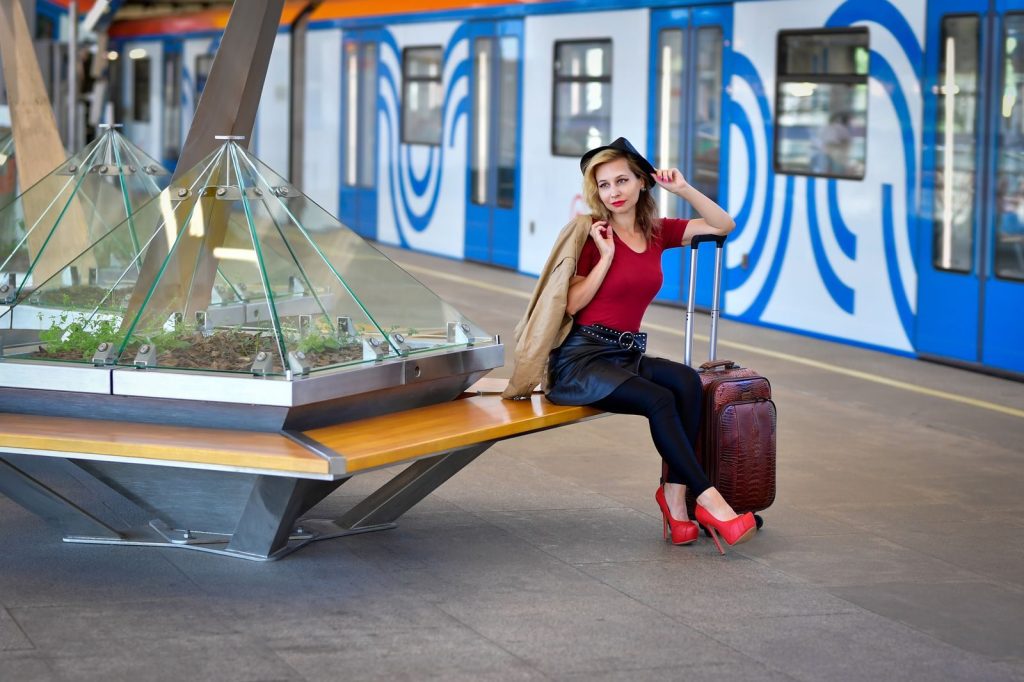 A stylish woman sits with luggage at a modern railway station, ready for travel.