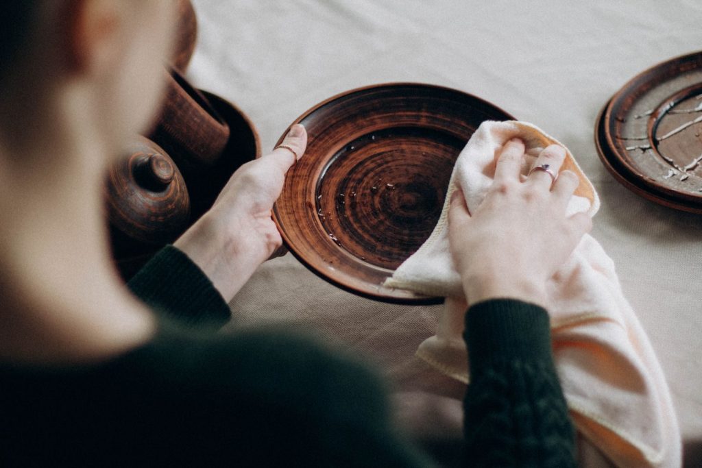 A woman cleaning a wooden plate on a table with a towel in a cozy setting.