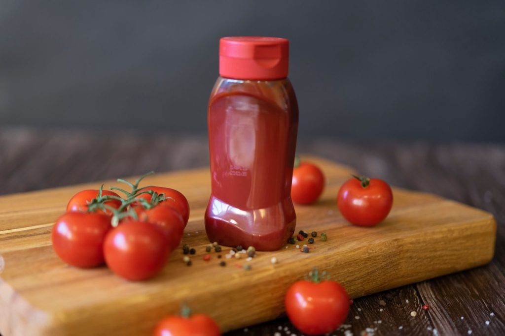 Close-up of tomatoes and ketchup bottle on a wooden board with peppercorns.