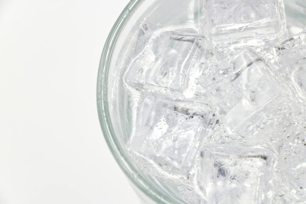 Close-up of a glass filled with sparkling water and ice cubes on a white background.
