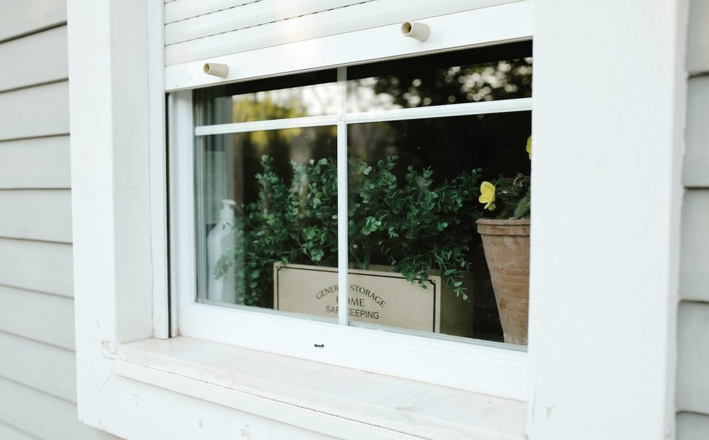 A serene garden view seen through a window with flower pots and storage box inside.