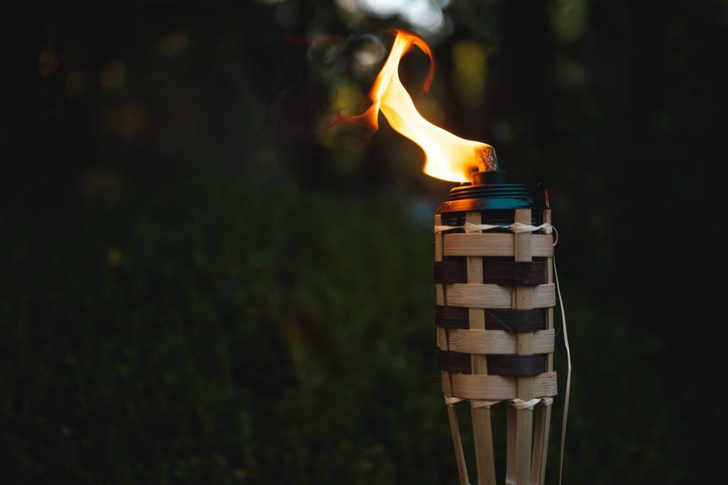 A close-up of a bamboo torch burning brightly in a dark outdoor setting.