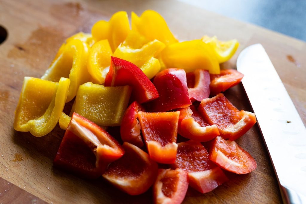 Brightly colored red and yellow bell pepper slices on a wooden cutting board with a knife.