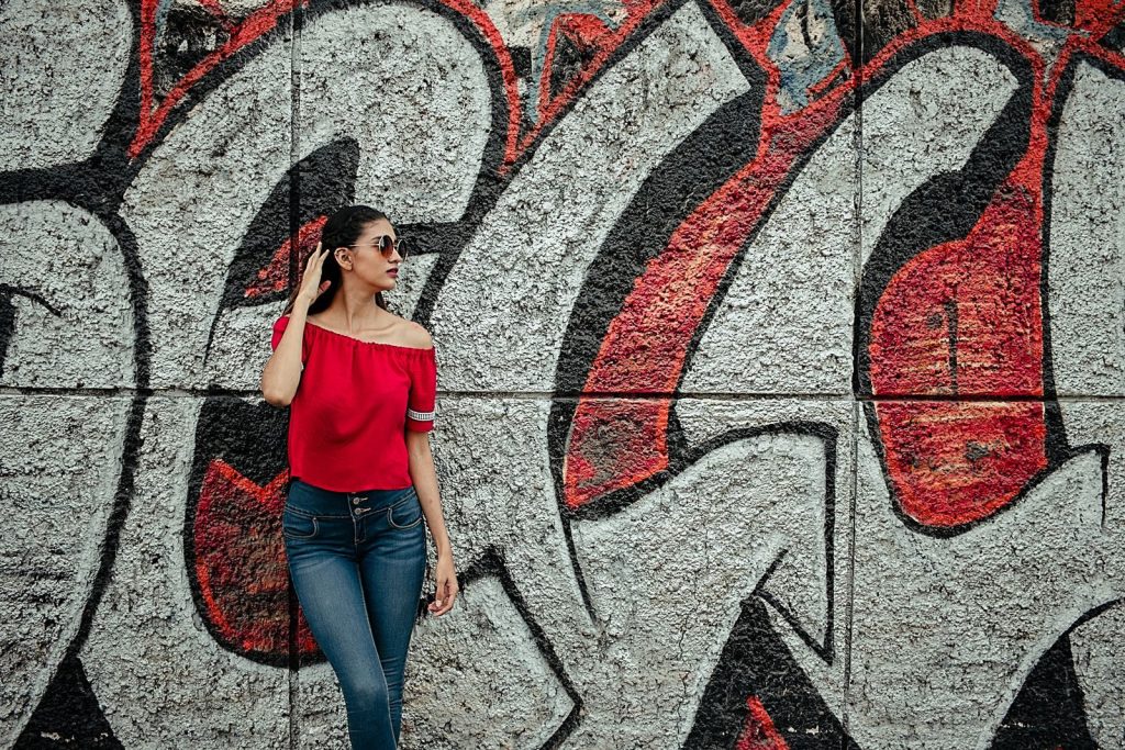 A fashionable woman in sunglasses poses confidently against a vibrant urban graffiti wall, showcasing street art.