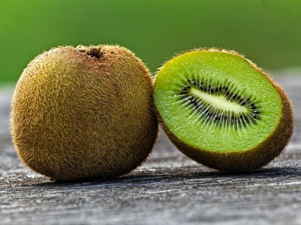 Detailed view of a whole and sliced kiwi fruit on rustic wooden table with blurred green background.