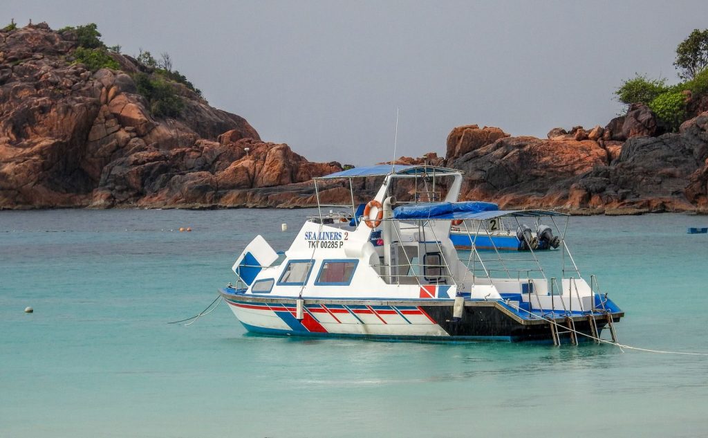 A vibrant boat anchored near rocky islands in a serene turquoise sea.
