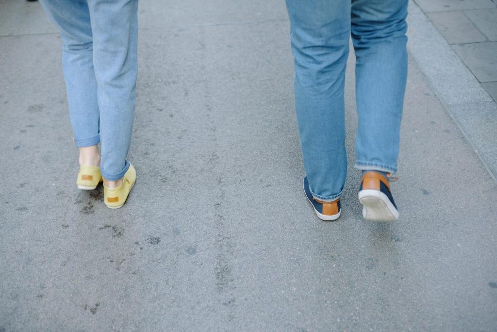 Two people walking casually on a city pavement in jeans and sneakers.