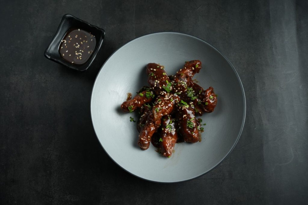 Delicious saucy chicken wings garnished with sesame seeds and herbs served on a plate with sauce.