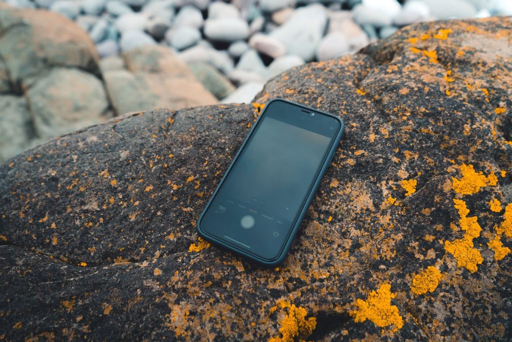 A smartphone placed on a textured rock with vivid orange lichen, capturing a rugged outdoor scene.