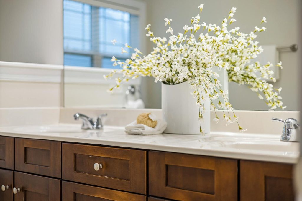 Bright bathroom with white flower arrangement, wooden cabinets, and mirror reflection.