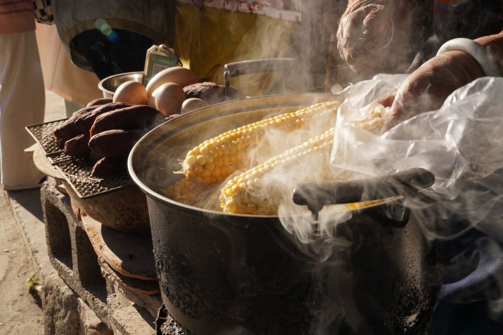 Steaming corn cobs being prepared by a vendor at an outdoor market, showcasing local street food culture.