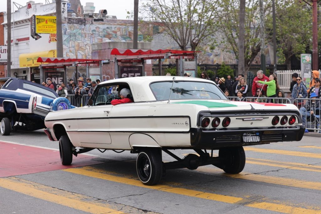 A retro lowrider car show with spectators in a vibrant urban street setting.