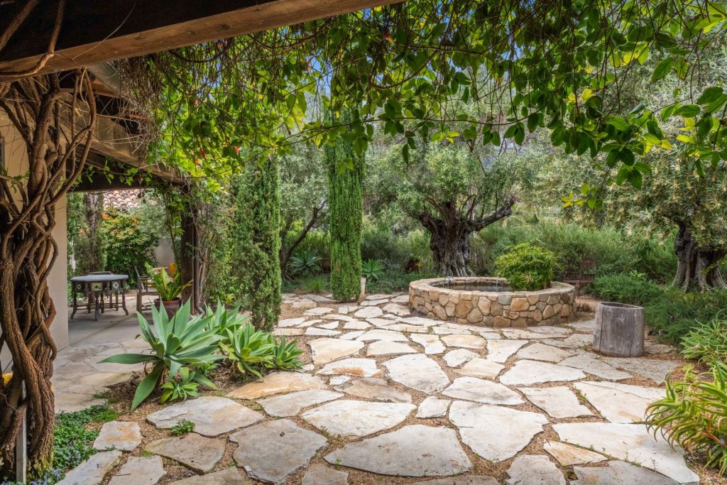 A tranquil garden with stone paths and lush greenery under a pergola.