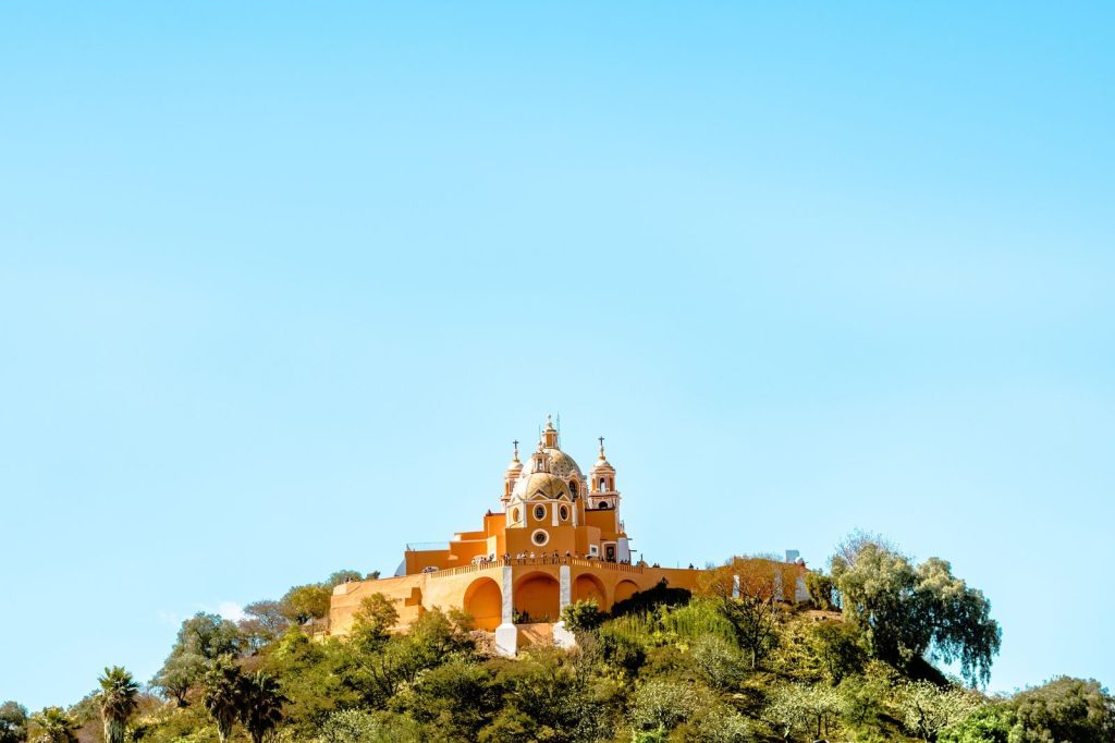 Sunlit Our Lady of Remedies Church on hill in Cholula, Mexico under clear blue sky.