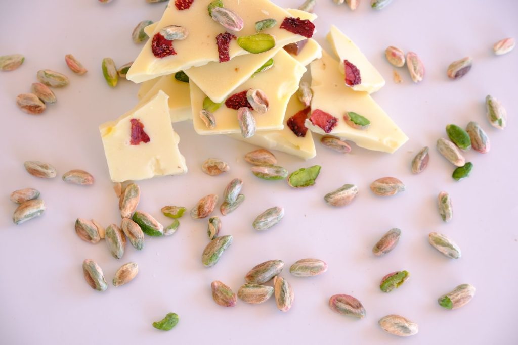 Flat lay of white chocolate bark with pistachios and dried berries on a light surface.