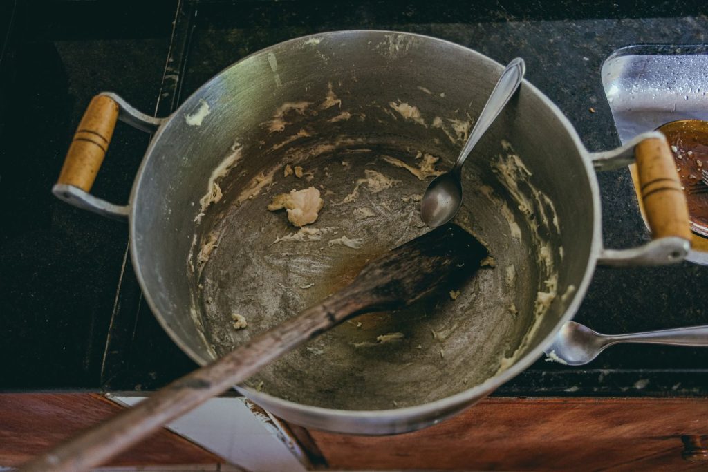 Aerial view of a cooking pot with leftover dough and utensils, highlighting kitchen preparation.