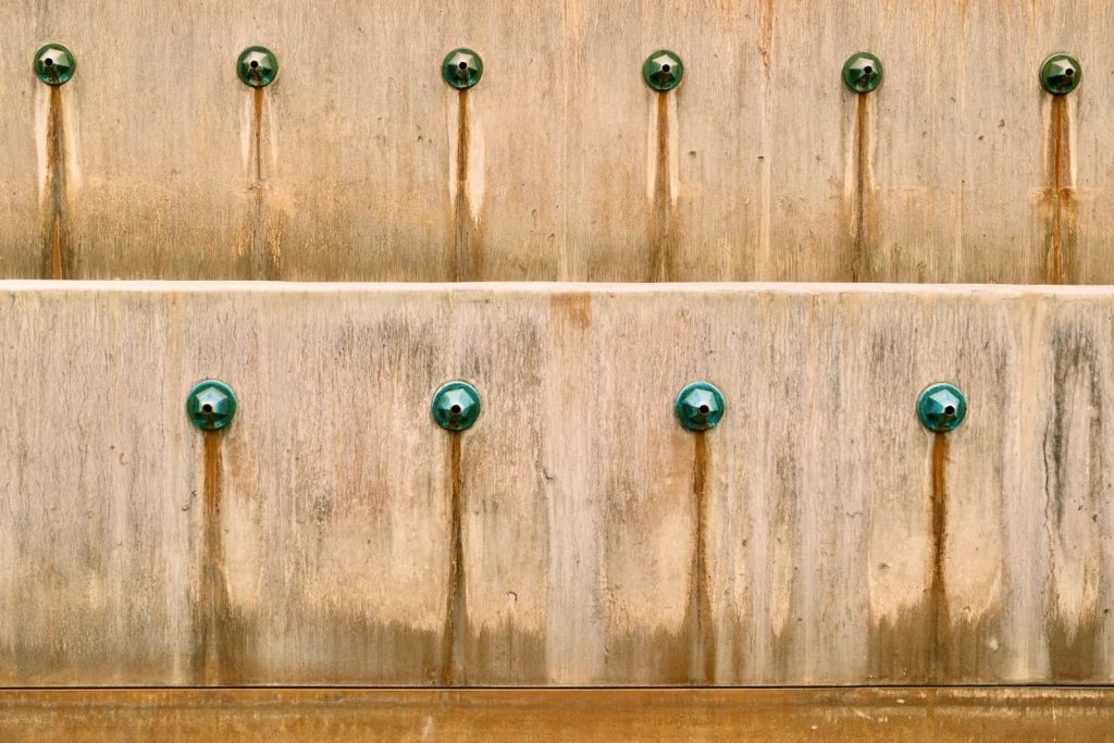 Weathered concrete wall detail with green rust stains highlighting aged texture and patterns.