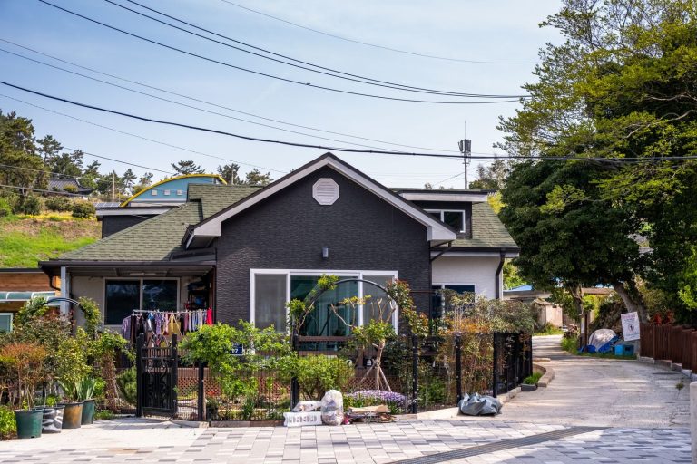 A charming suburban house with a lush front garden and laundry hanging outside on a sunny day.