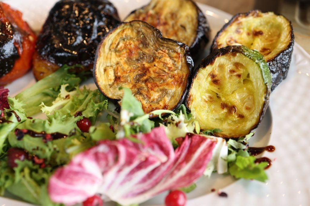 Close-up of roasted vegetables and mixed salad served on a white plate, perfect for healthy meals.