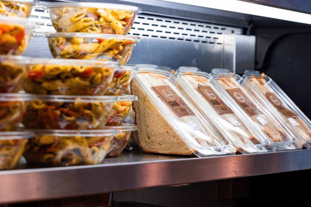 Delicious ready-to-eat pasta salads and sandwiches displayed in a store fridge.