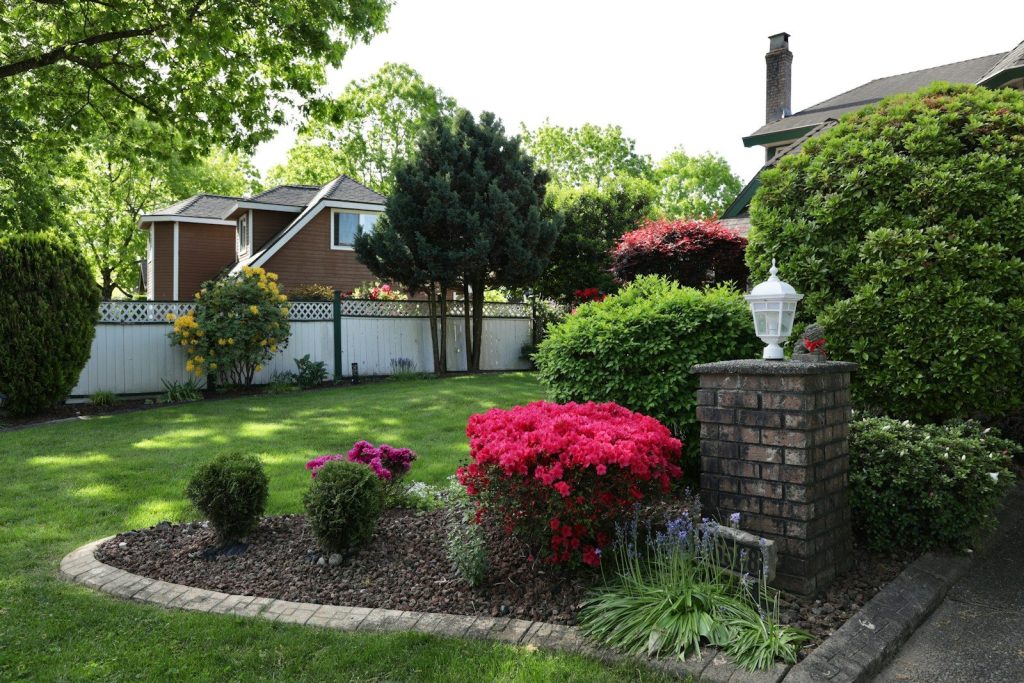 Lush green garden with blooming flowers and brick lamp post.