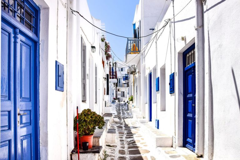 Narrow Greek alley with traditional white and blue buildings on a sunny day.