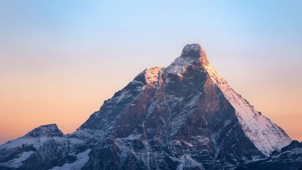 A stunning view of the Matterhorn mountain at sunrise, casting a golden glow on its snowy peak.