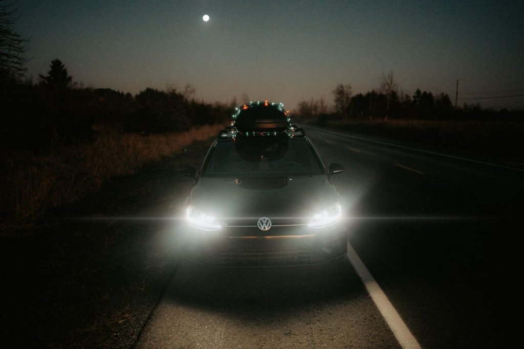 A car travels on a dark, rural road at night, illuminated by full moonlight.
