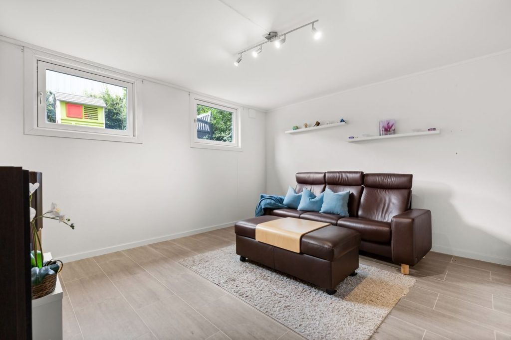 Spacious minimalist living room featuring a brown leather sofa and simple decor.