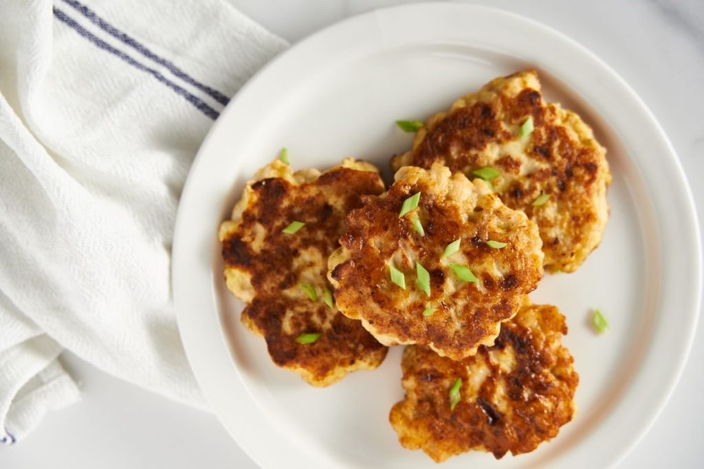 Top-down view of golden homemade chicken patties garnished with herbs on a white plate.