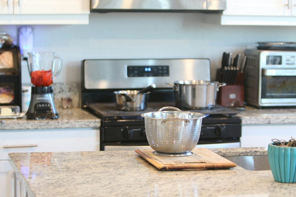 A modern kitchen with a colander, stove, and blender.