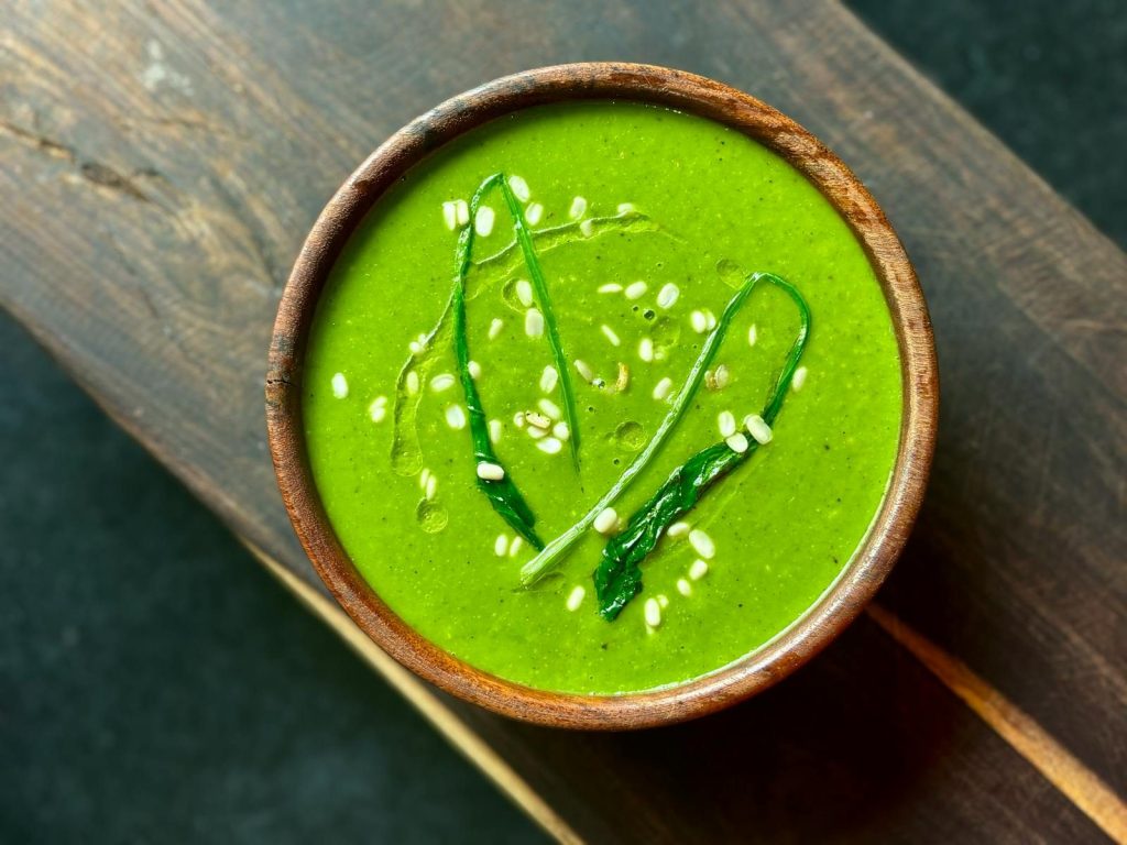 Delicious spinach soup garnished with sesame seeds and greens, served in a rustic wooden bowl.