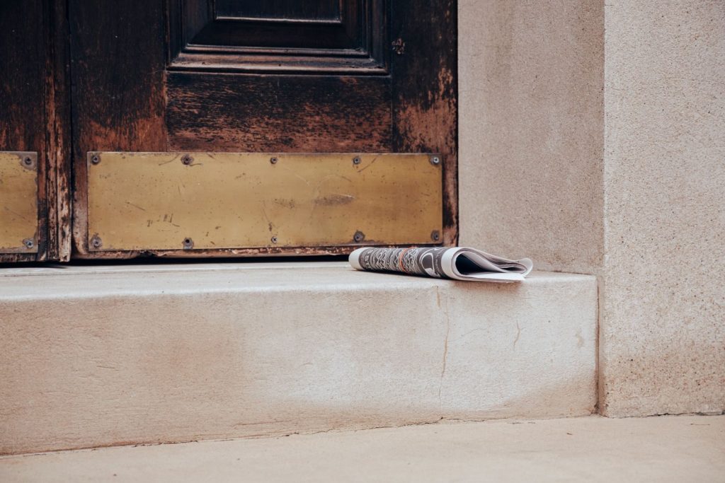 Folded newspaper on a stone step in front of a classic wooden door, urban street scene.