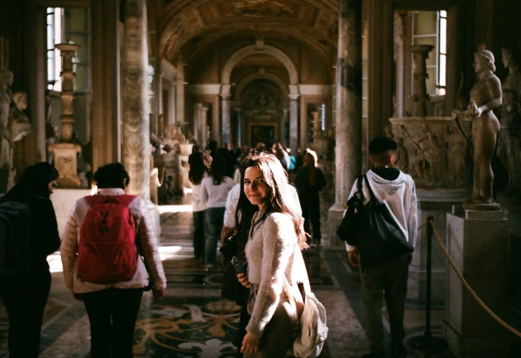 Tourists exploring the historic corridors of the Vatican Museums, surrounded by ancient sculptures and art.